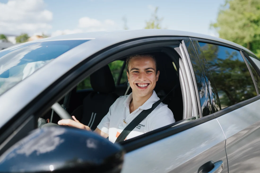 Ein lachender Fundraiser des Bayerischen Roten Kreuzes sitzt am Steuer eines Autos