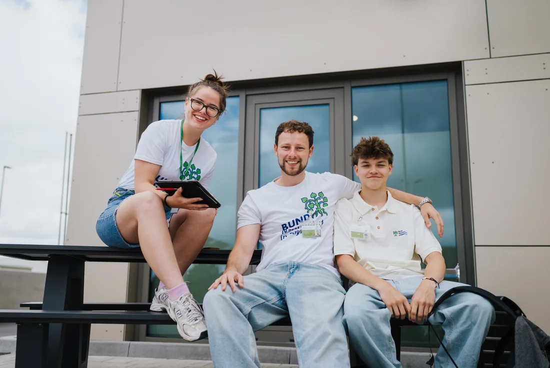 Drei Fundraiser in Shirts vom Bund Naturschutz sitzen lachend auf einer Bank