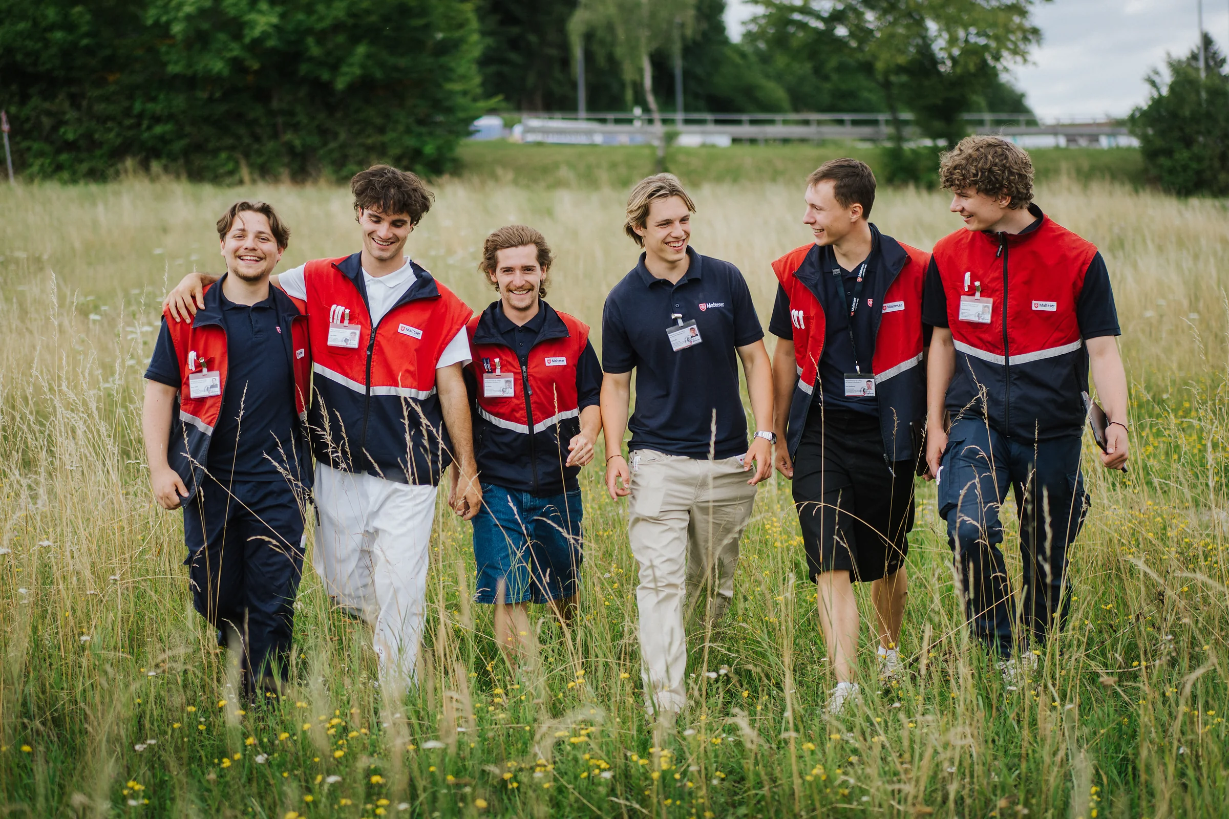 Eine Crew Fundraiser geht Arm in Arm durch eine Sommerwiese